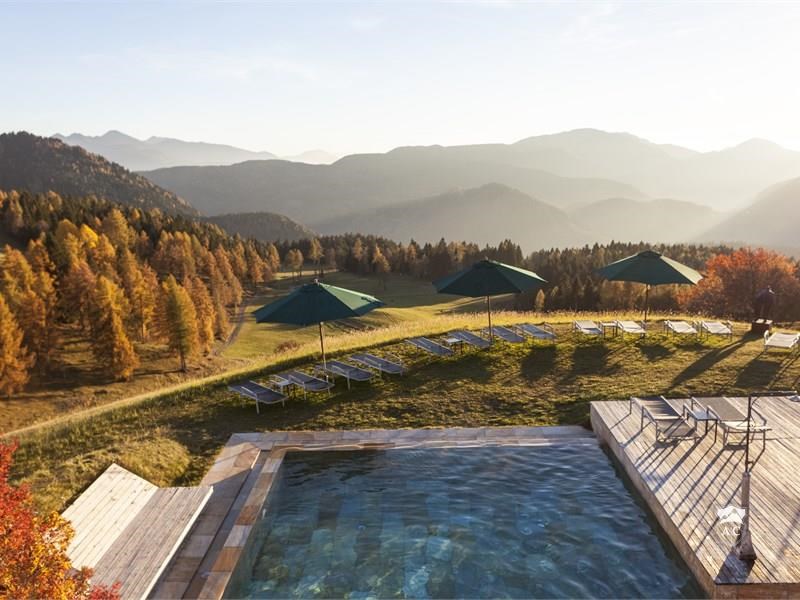 Blick über den Pool mit Terrasse, Liegewiese und umliegender Bergwelt